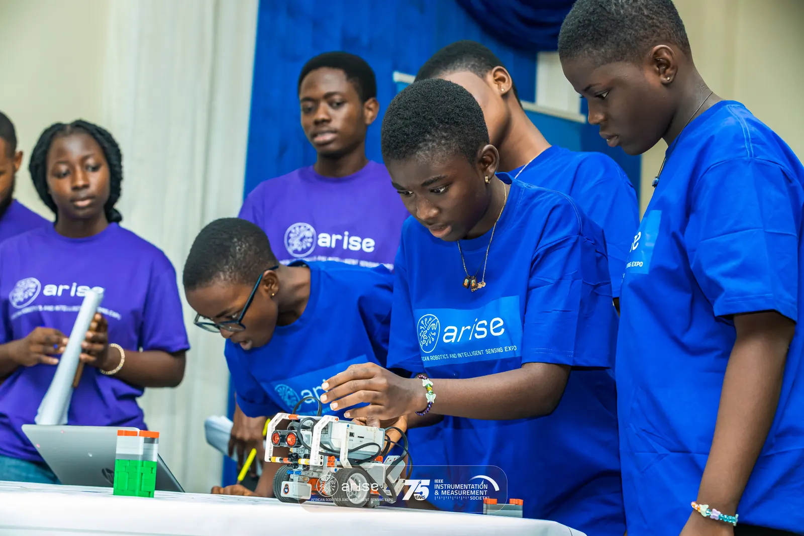 Students in ARISE t-shirts testing a LEGO robot at the ARISE robotics competition