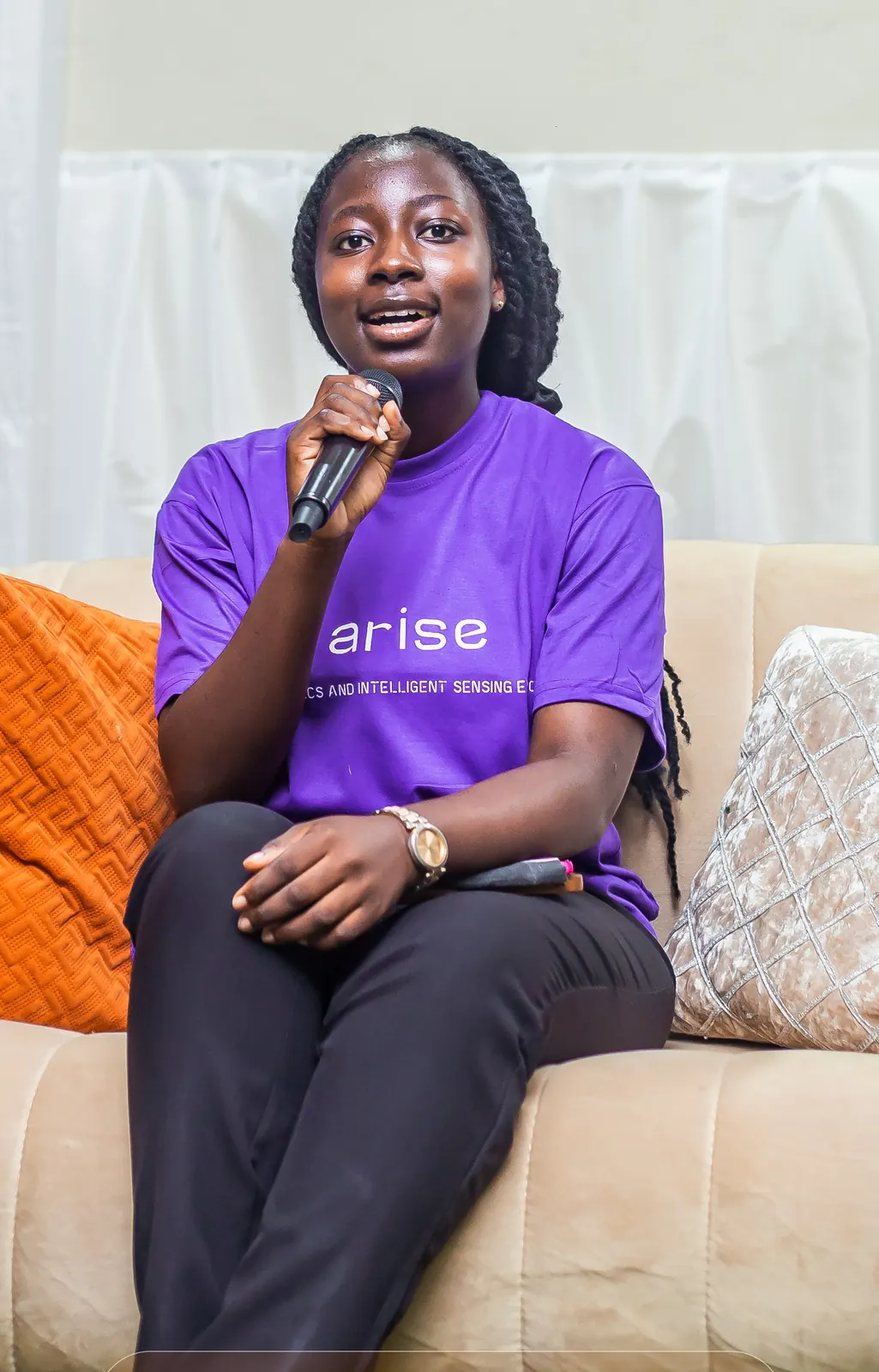 Kobi speaking into a microphone on a panel at ARISE, wearing an ARISE t-shirt