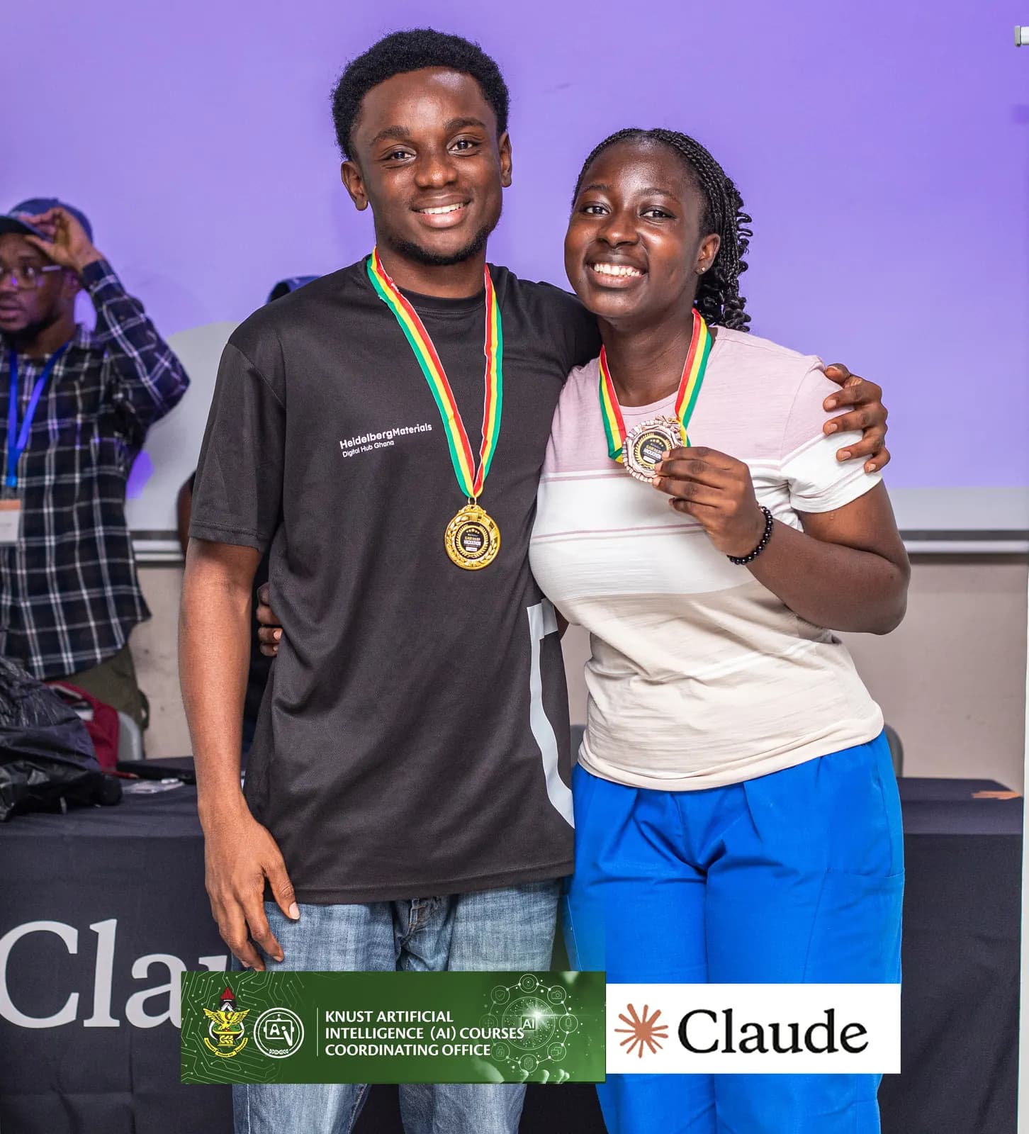Kobi and a teammate wearing medals beside a Claude banner at the KNUST Claude hackathon