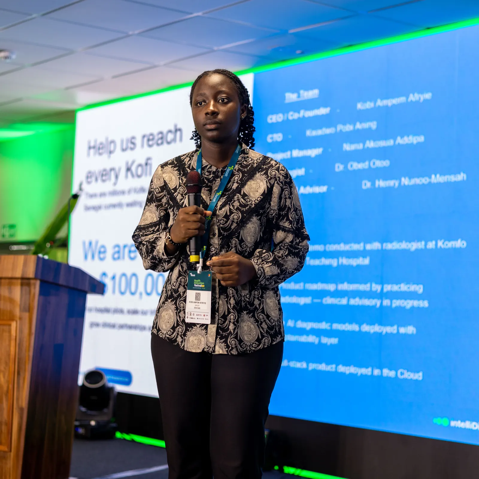 Kobi on stage with a microphone, presenting the IntelliDiag team slide at HIFest 2026