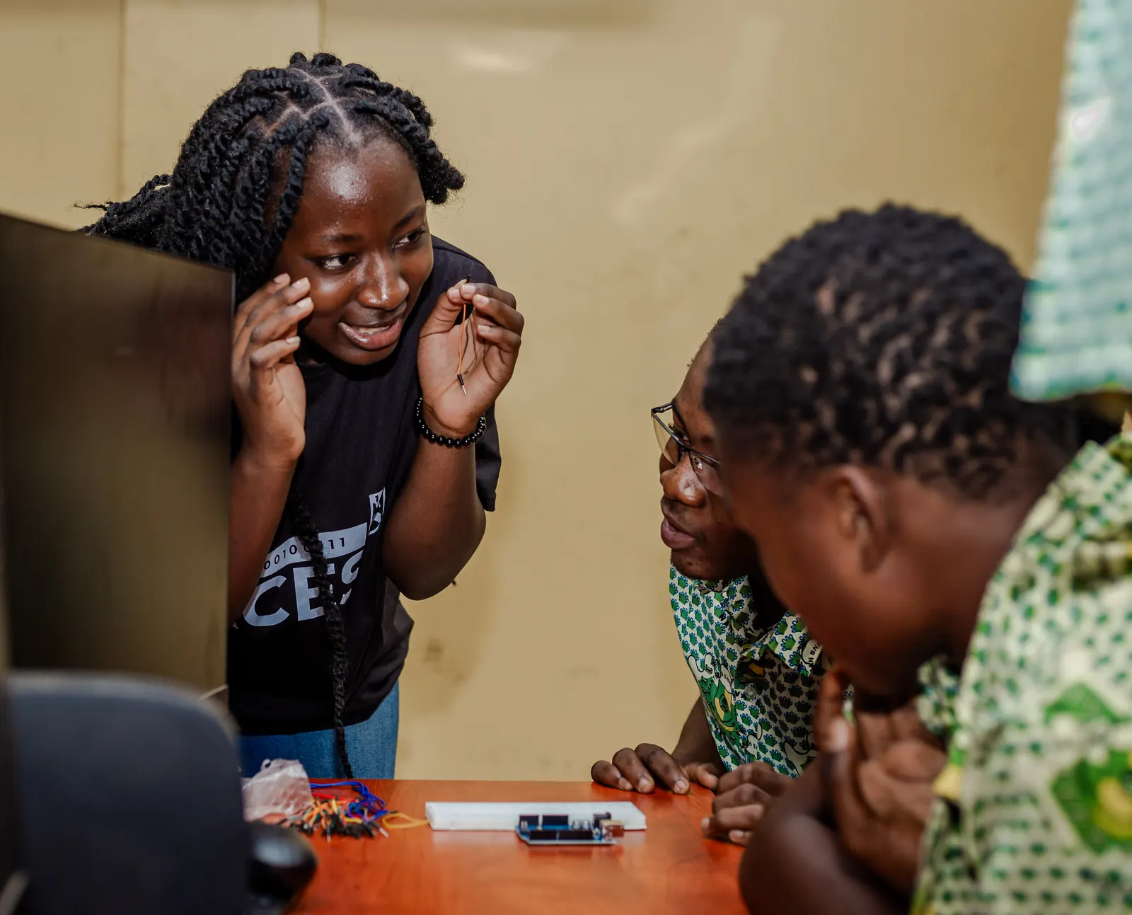 Kobi holding a jumper wire and explaining an Arduino circuit to two students